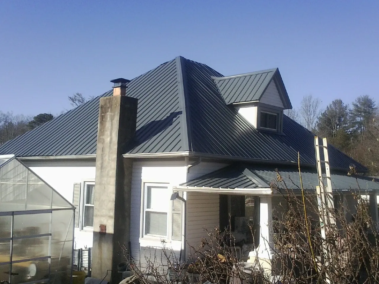 Dark blue standing seam metal roof on a white farmhouse with dormer — Slate & Tile Roof Repair by Roofing Brothers in Winston-Salem
