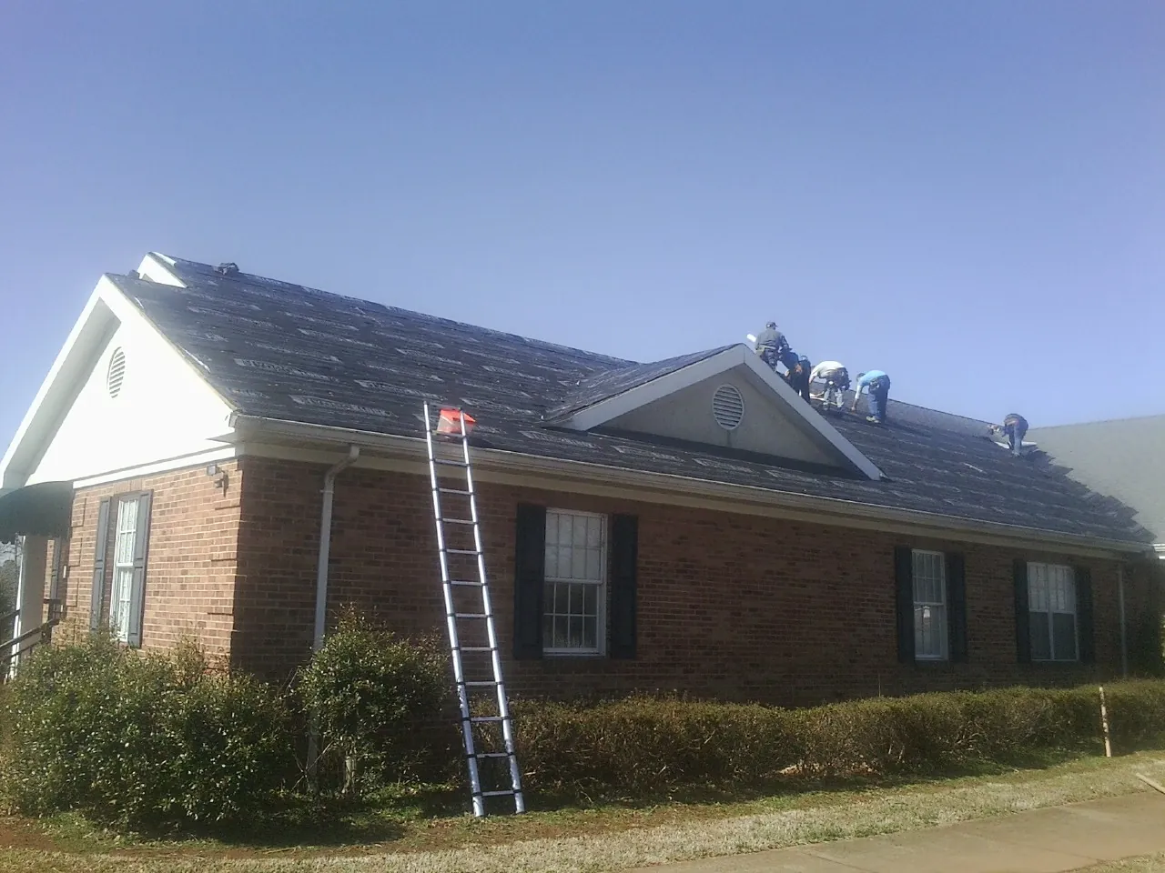 Crew tearing shingles off a brick ranch roof with a ladder set — Metal Roof Repair work by our crew in Winston-Salem