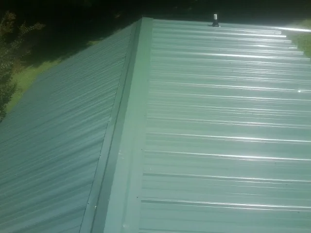 New green metal panels meeting at the ridge of a roof — Flat Roof Repair work by our crew in Winston-Salem