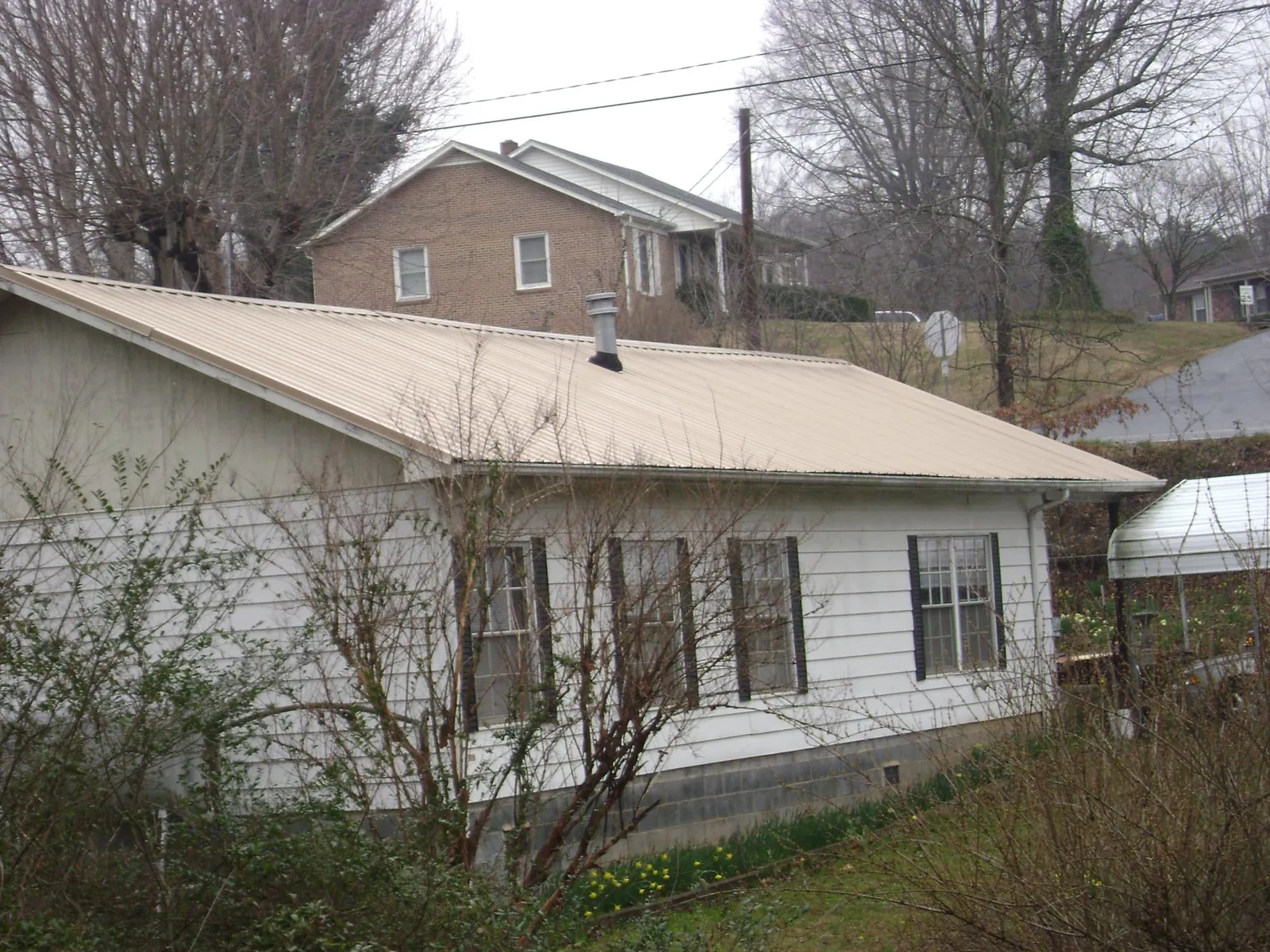 Tan metal roof on a white sided house set into a hillside — Commercial Roofing by Roofing Brothers in Winston-Salem