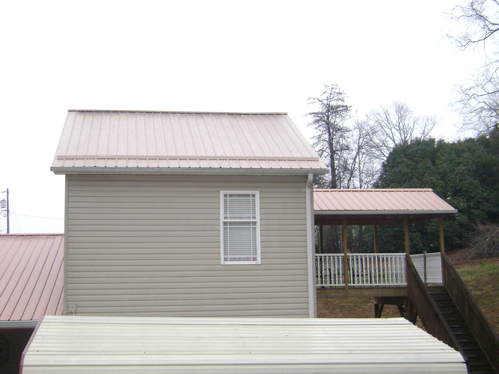 Tan metal roofs on a two story addition and attached porch, from a Roof Replacement job in Winston-Salem